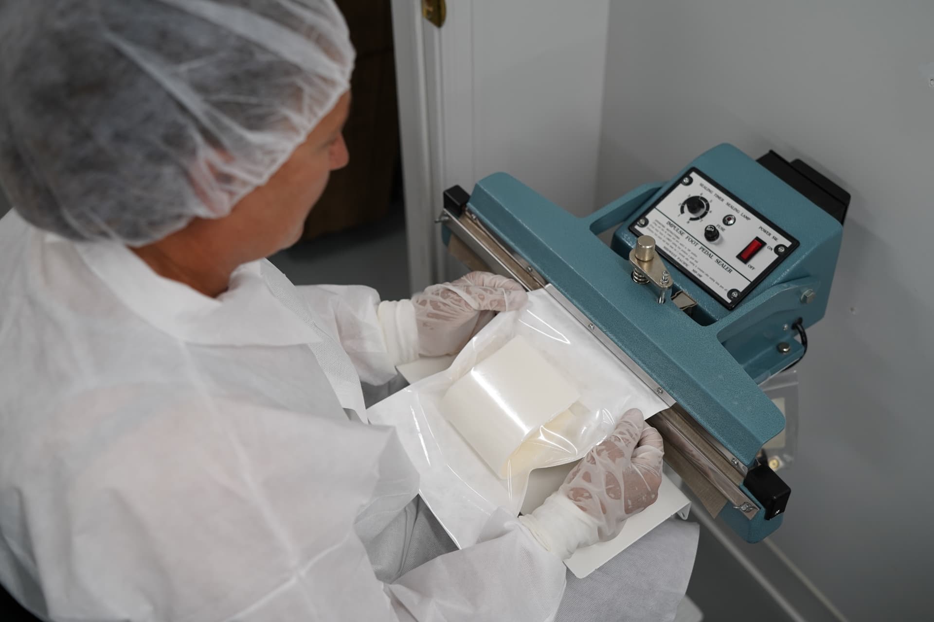 Technician performing impulse pouch sealing in cleanroom garments